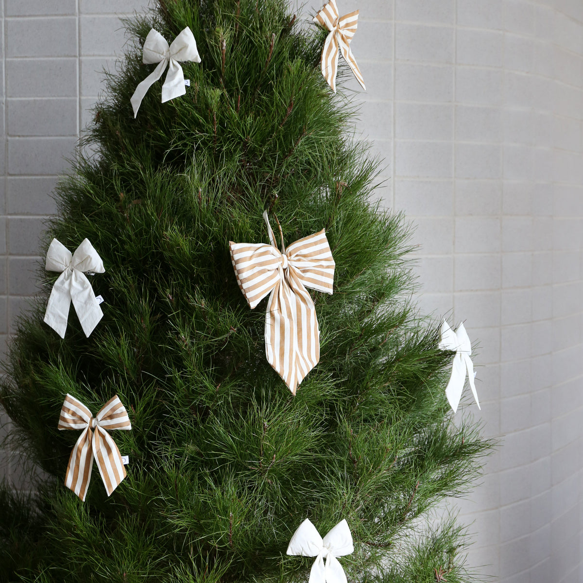 Decorative Christmas tree with white and gold ribbons against a gray tiled wall.
