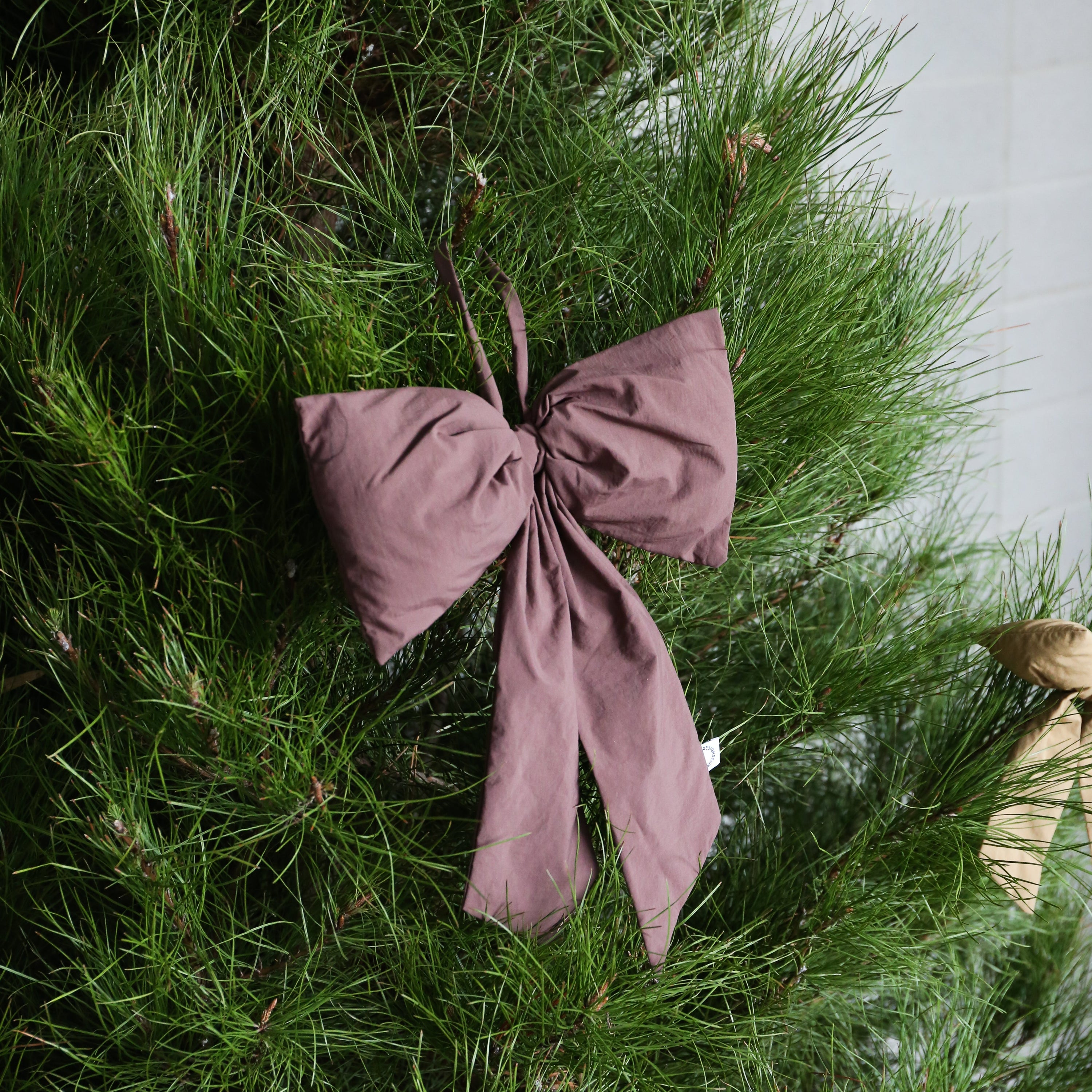 Burgundy bow ornament on a Christmas tree with a white wall background