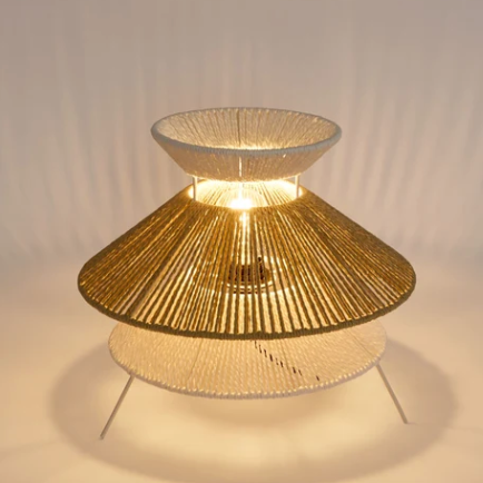 A three-tiered table lamp with a woven gold and white design, illuminated from within to cast a warm glow. 