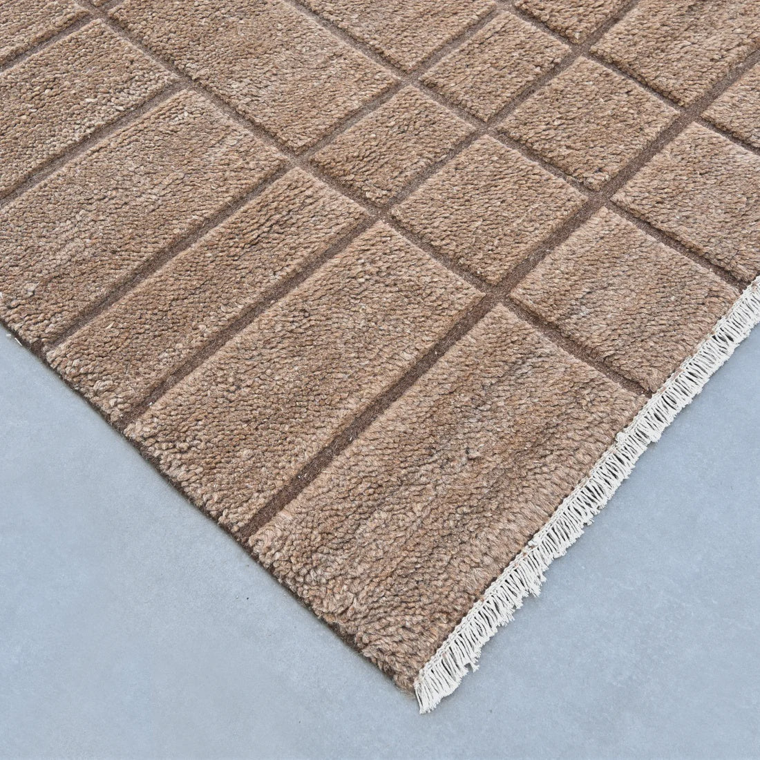 Textured brown rug with linear pattern with cream fringe on a light blue background