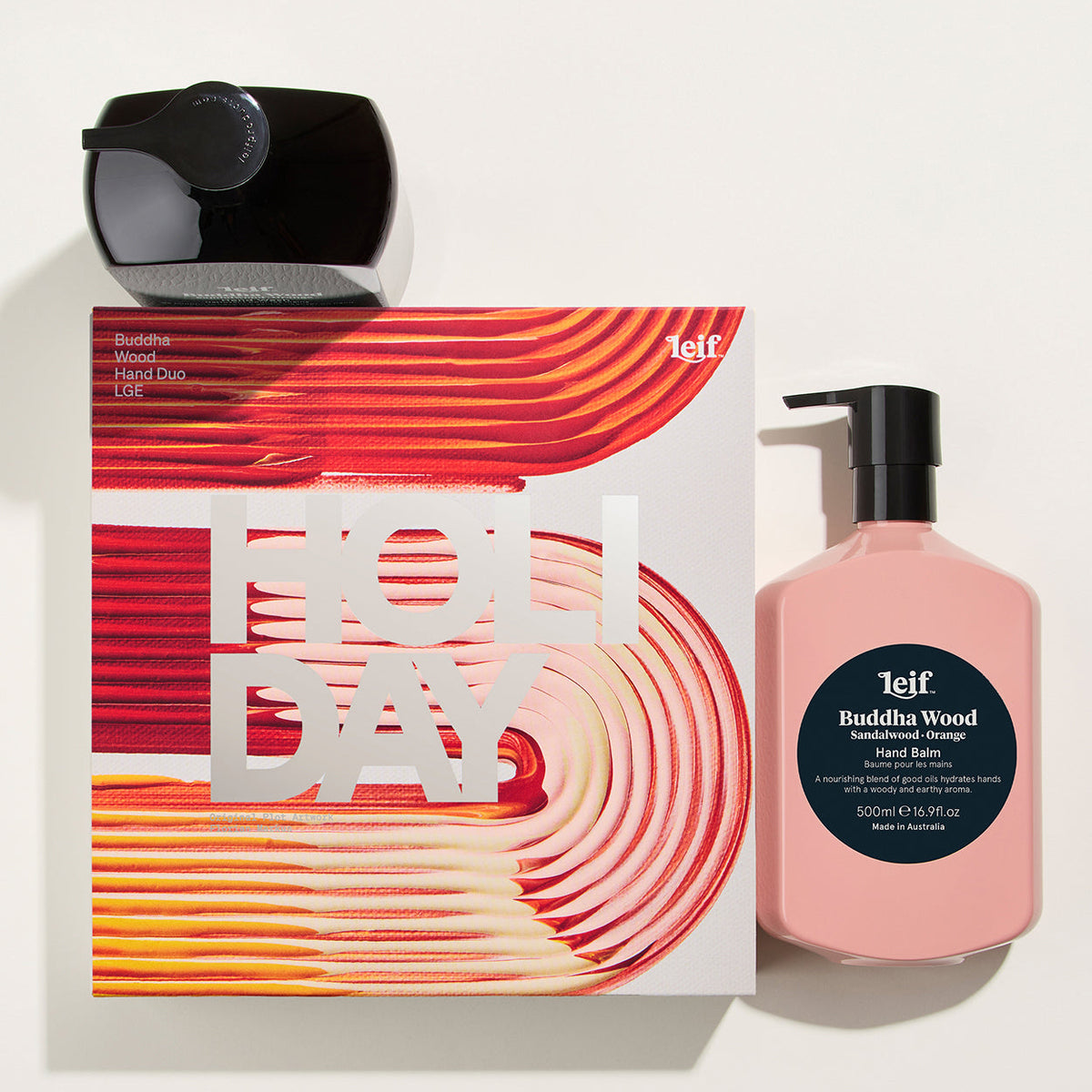 Teif Holiday Buddha Wood hand and body care gift set on a light beige background, featuring a pink pump bottle, a white box with red and orange wavy patterns, and a black cylindrical container.
