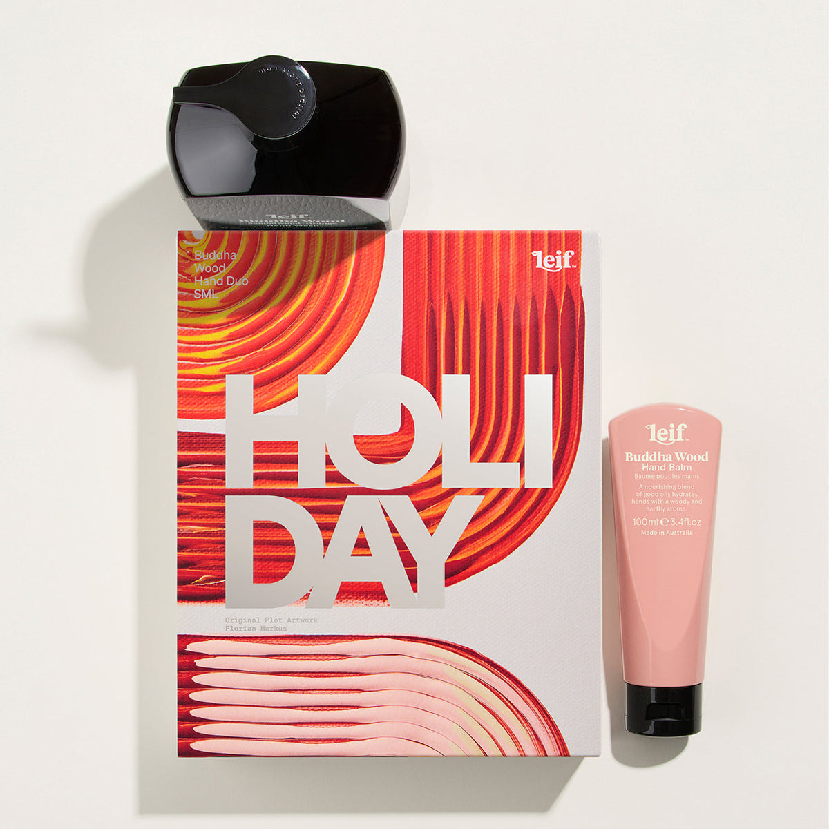 A 1elf Holiday gift set featuring a pink and red patterned box with large white 'HOLIDAY' text, a black spray bottle, and a pink tube of exfoliating body wash on a clean white background.