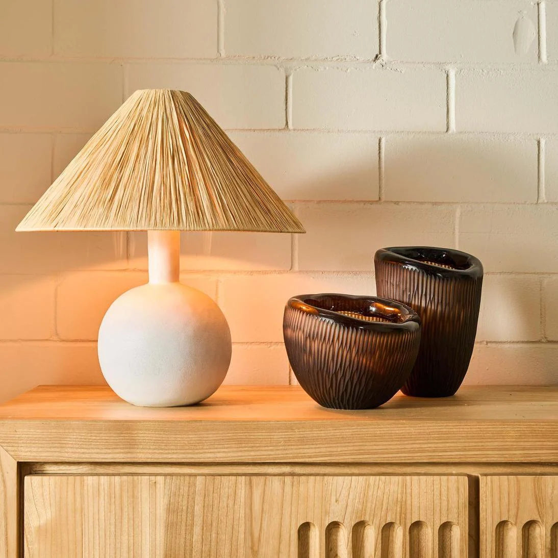 White ceramic lamp with a textured shade on a wooden surface against a tiled wall.