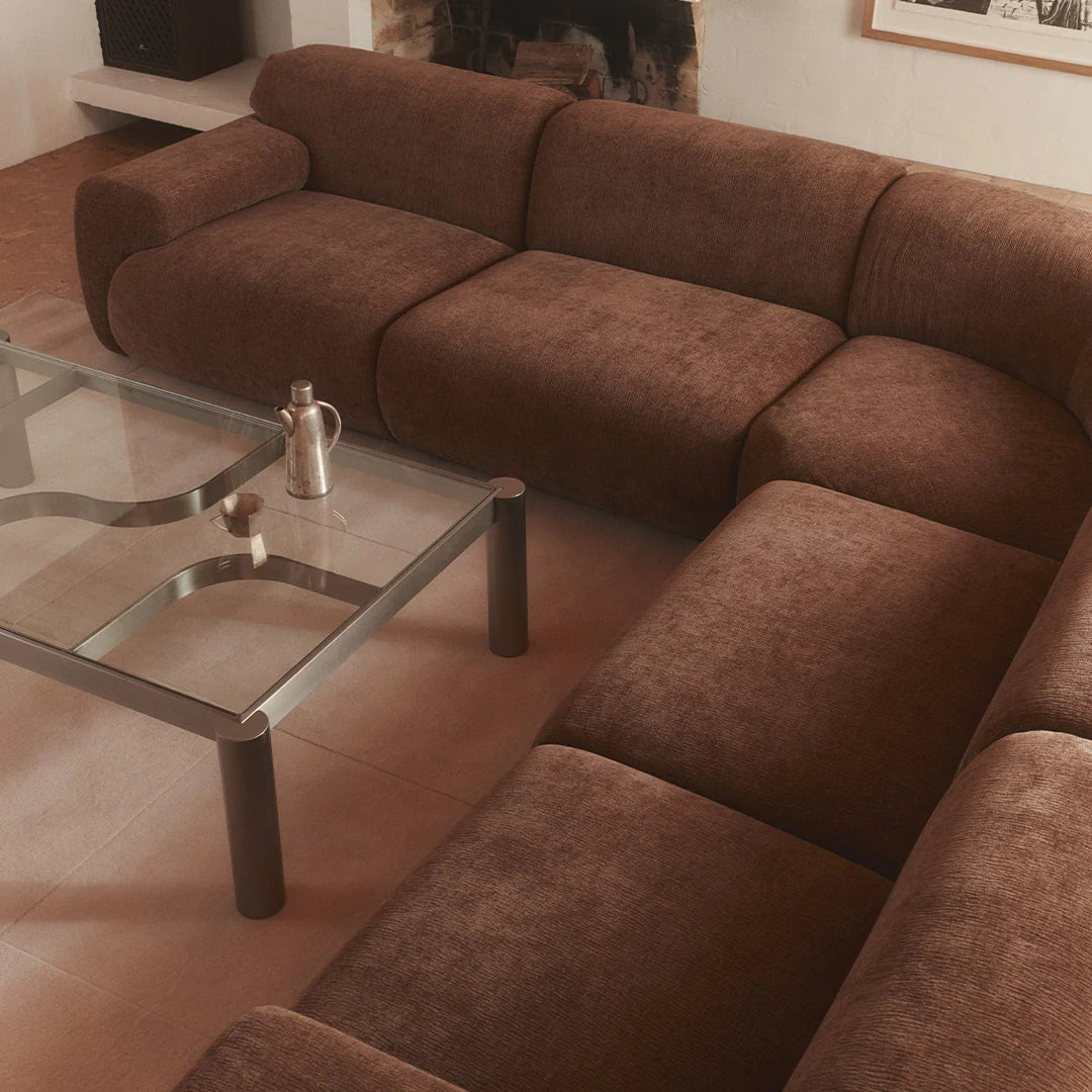 A brown upholstered sectional sofa arranged in an L-shape in a living room, with a glass-top coffee table in front.
