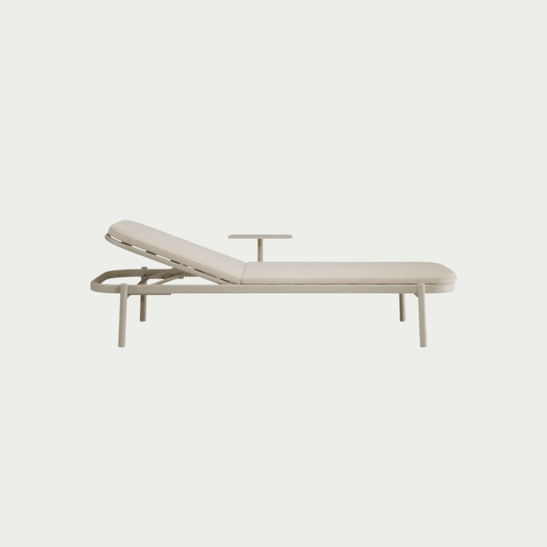 A modern outdoor chaise lounge chair with a light beige cushioned frame and a small matching side table, shown against a solid off-white background.