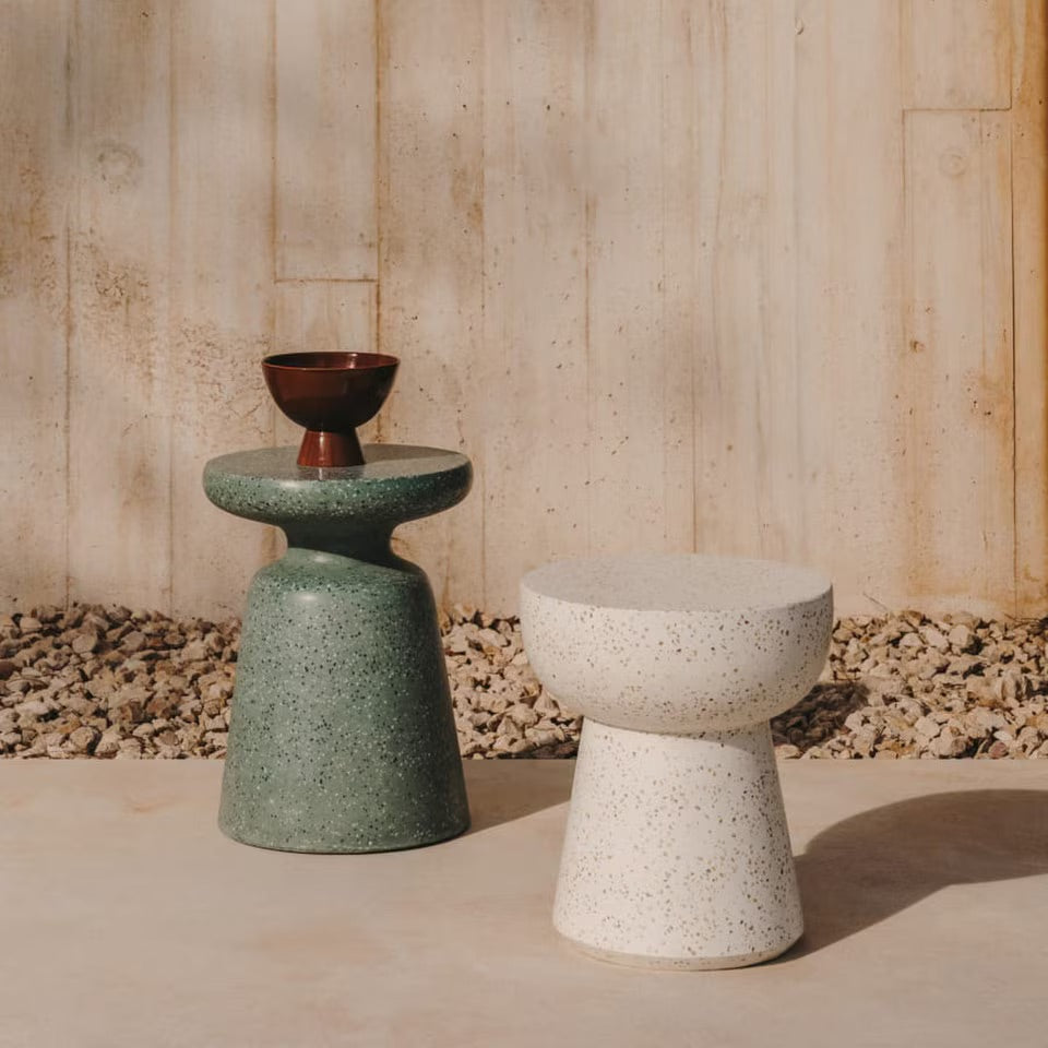 Two stone-styled stools, one green and one white, against a wooden wall.