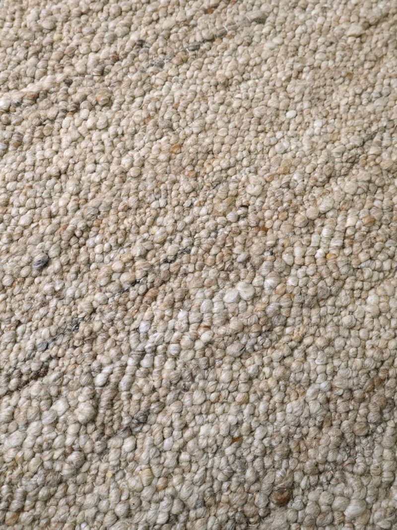 A close-up texture shot of a loop-pile carpet or rug in a speckled beige, cream, and light gray colorway with small dark flecks.