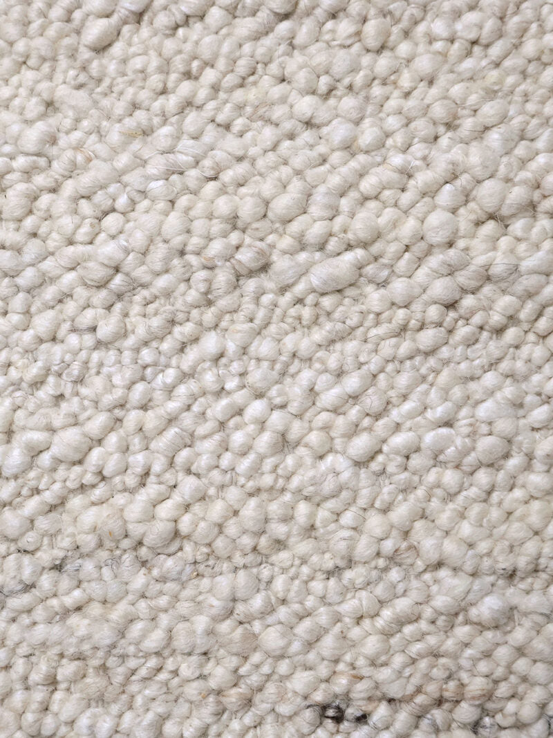 A close-up texture shot of a chunky, looped wool or mohair rug in a warm off-white or cream color.