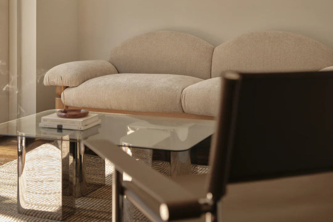 Beige sofa in a living room with a glass coffee table and a chair. Glass coffee table. chrome and glass styling. glass top coffee or side table