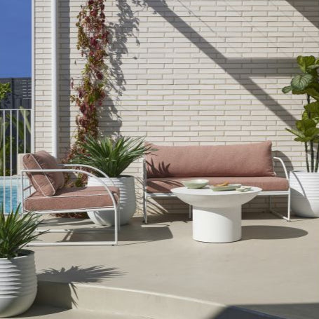 Reeve Outdoor 2 Seater Sofa in Coral Pink, white metal frame with plush cushions and white piping, styled outdoors.