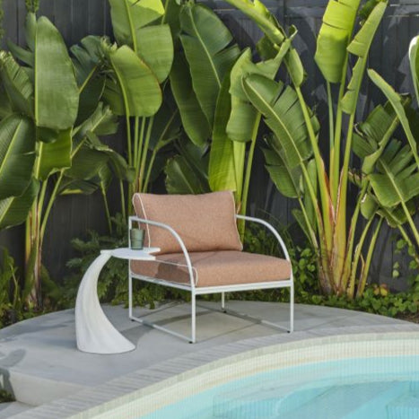 Reeve Outdoor Armchair in Coral Pink, white metal frame with plush cushions and white piping, styled outdoors.