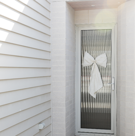 large White bow on a glass door with light gray siding.