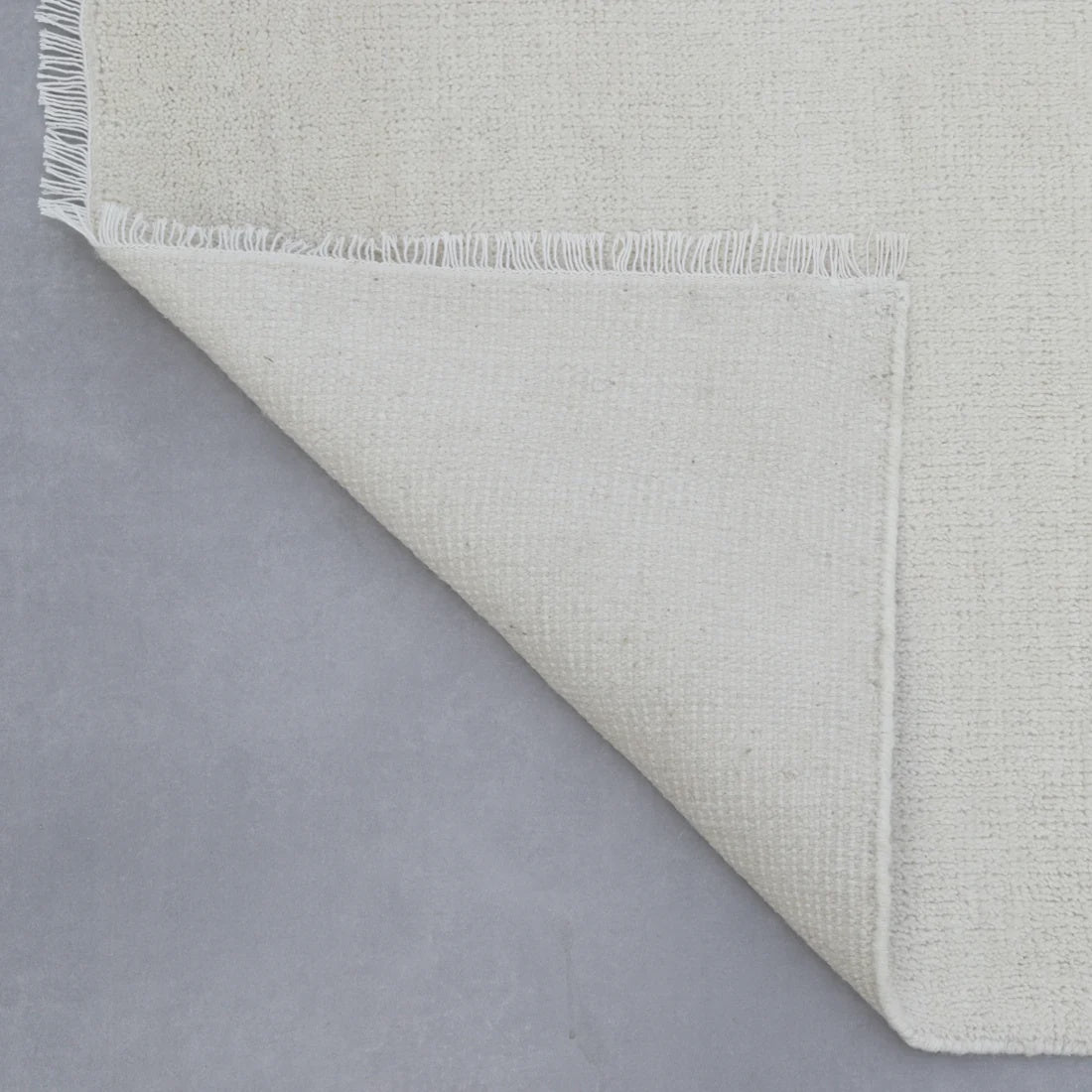 Close-up of a textured gray rug corner on a matching gray background