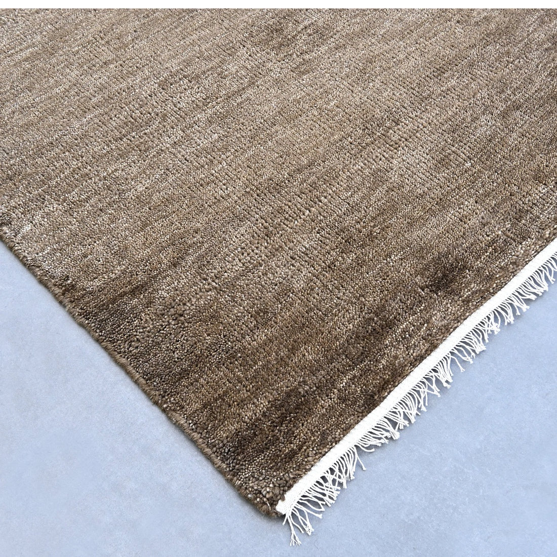 Brown textured rug with frayed edge on a light blue background