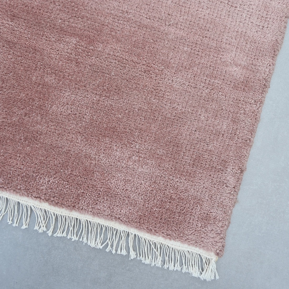 Pink textured rug with white fringe on a gray background