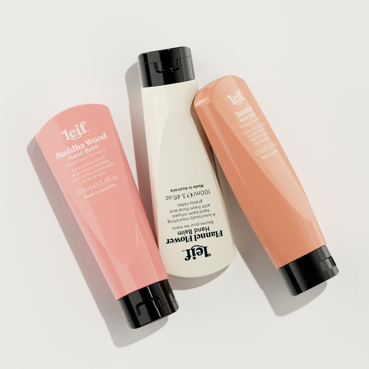 Three Telf hand care bottles arranged diagonally on a light gray background: a pink Buddha Wood hand wash, a white Emerald Flower hand wash, and a peachy-orange hand wash, all with black caps.