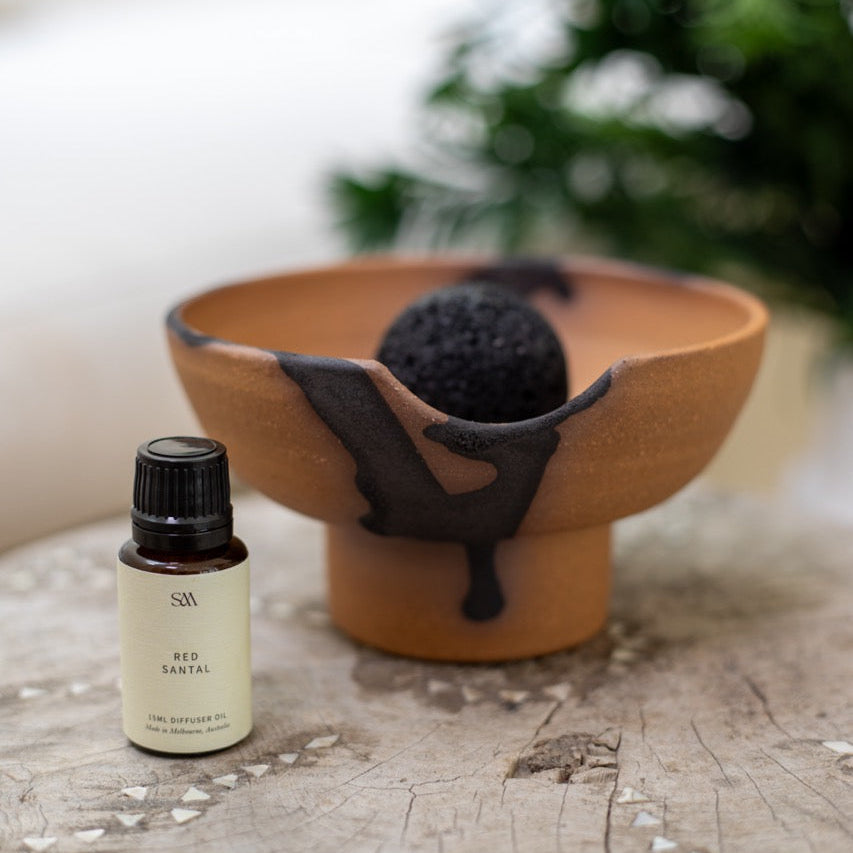 Diffuser with volcanic rock sphere and fragrance oil bottle on styled surface