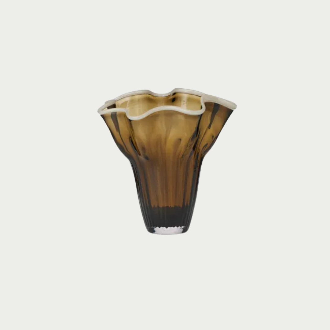A fluted amber glass vase with a wavy rim, featuring a gradient from golden brown to dark brown and black at the base, set against a solid off-white background.