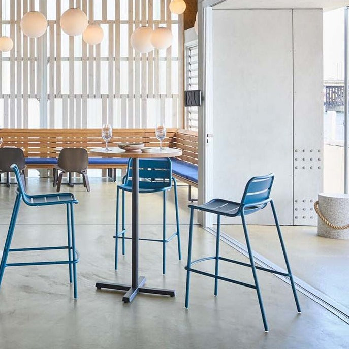 blue high stools in an outdoor setting with a wooden table and benches in the background.
