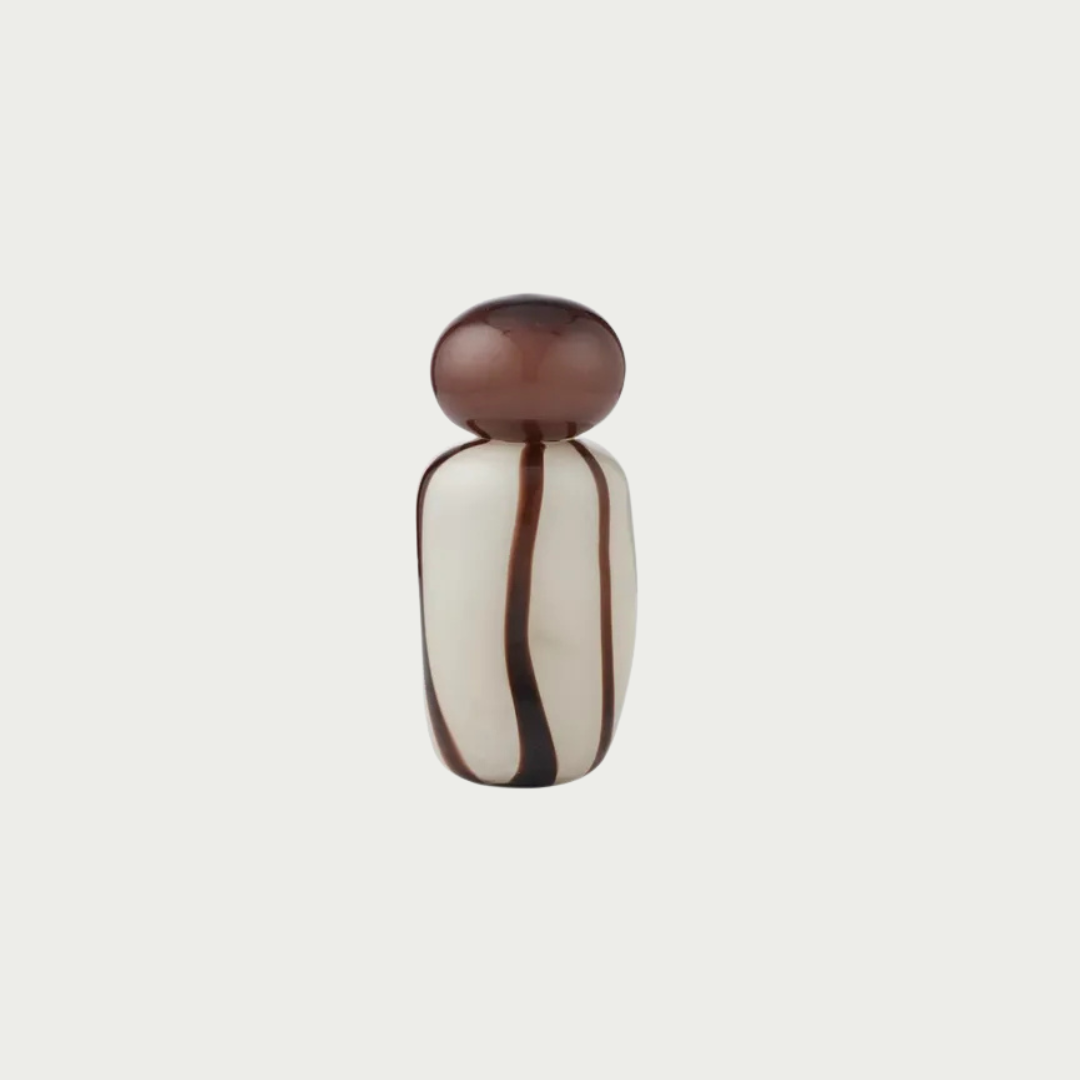 A small decorative bottle or vial with a rounded dark brown cap and a bulb-shaped body featuring vertical dark brown stripes on an off-white base, centered against a light gray background.