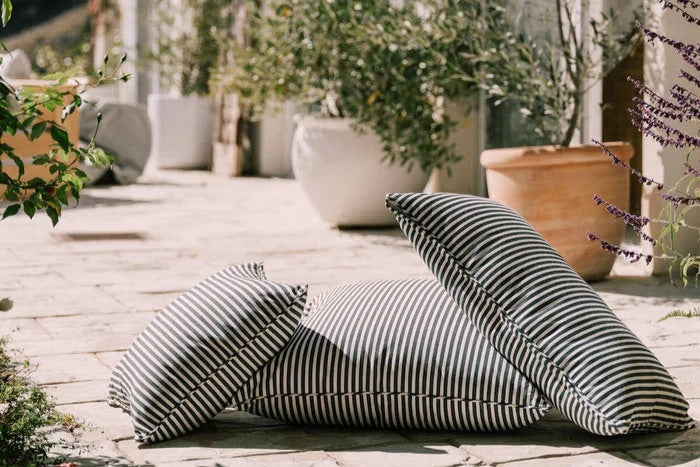 Striped outdoor cushions on a wooden deck with plants and a building in the background. Outdoor cushions. alfresco cushions