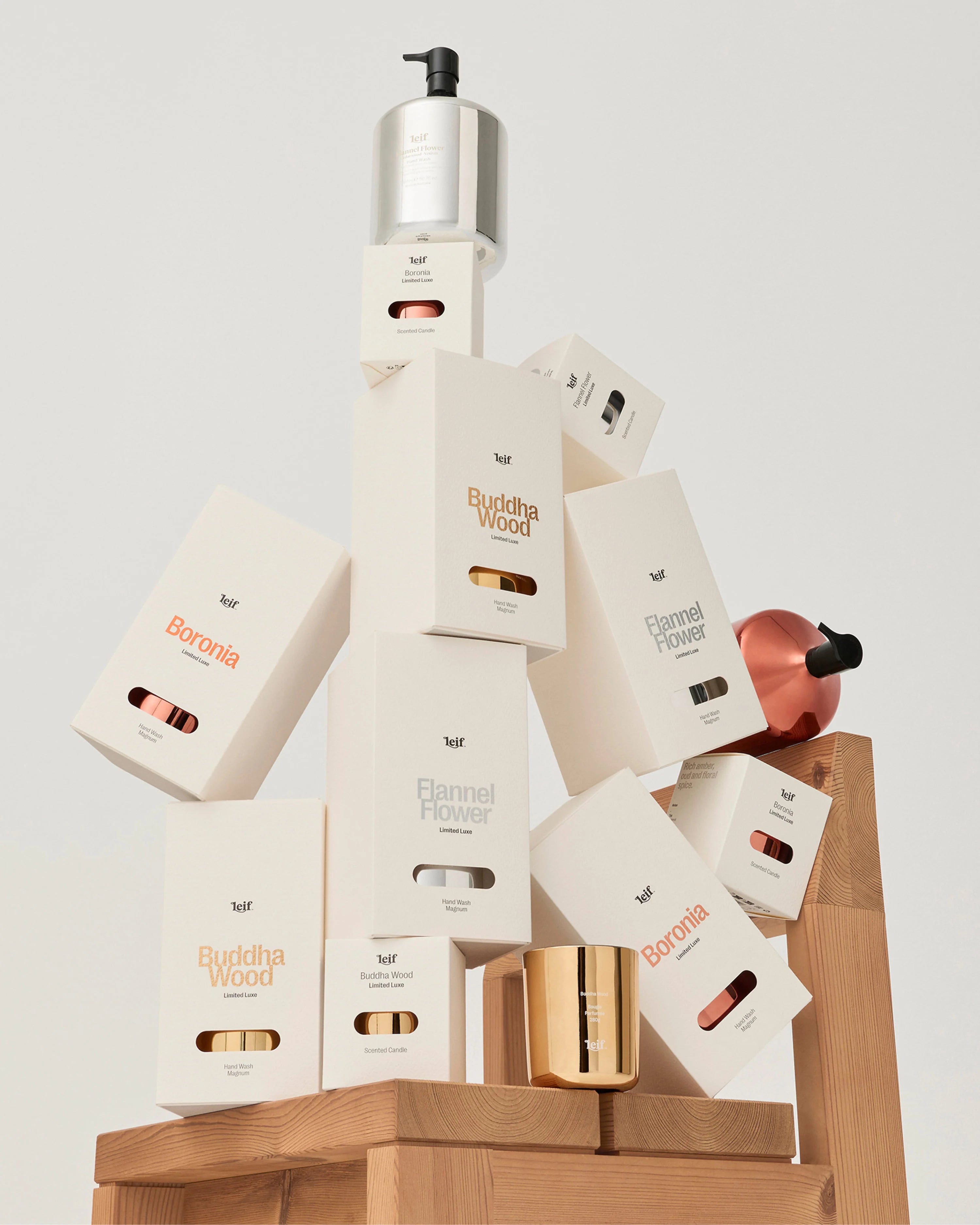 A styled product display featuring multiple white and metallic product boxes from the brand huf, including 'Boronia' and 'Flamel Flower' scents, arranged on a wooden block against a light gray background.