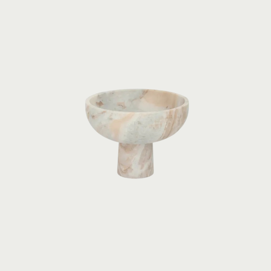 A small pedestal bowl made of pale marble with soft pink and gray veining, centered on a plain light gray background.