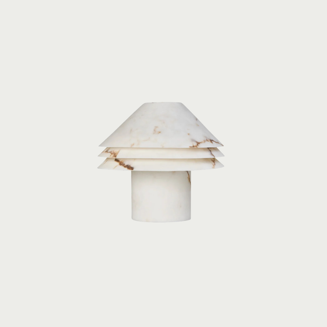 A small modern table lamp made from layered white marble with subtle warm brown veining, featuring a tapered top and cylindrical base, centered on a solid off-white background.